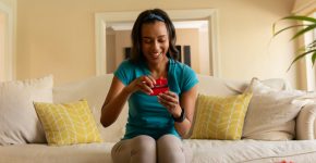 Happy young african american woman opening valentine's gift box sitting on sofa at home