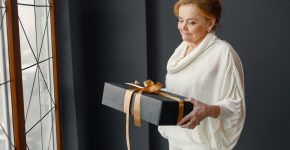 Old woman standing indoors holding a gift box